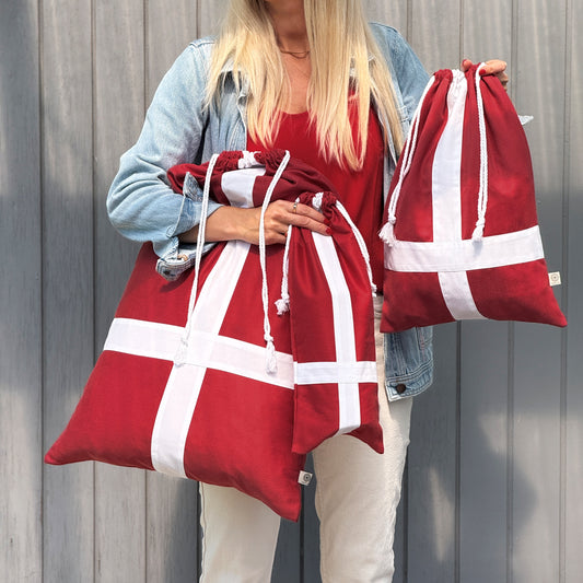 Person holding two red drawstring bags with white stripes against a wooden background