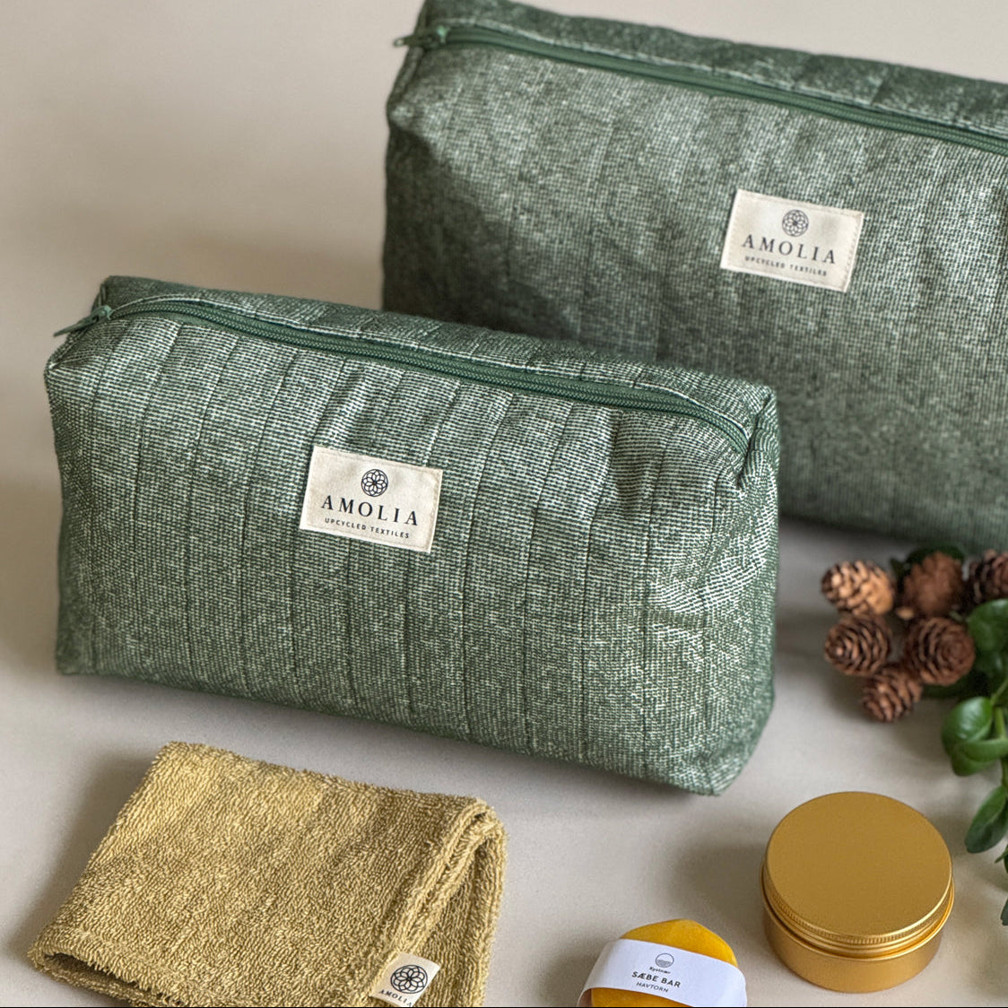Two green textured bags with 'Amolia' branding and small containers on a light background.